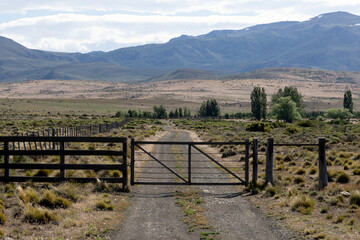 Fototapeta premium A simple wooden gate and after it a narrow road into the Patagonian steppe
