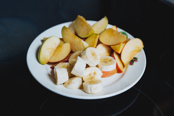 On a pristine white plate, there is a delightful arrangement featuring freshly sliced bananas alongside vibrant apple slices, creating an appealing and healthy snack option