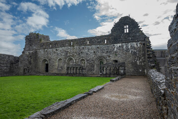 Ruins of an old stone building with arched windows at Abbey Cong, Ireland, surrounded by a lawn under a partly cloudy sky