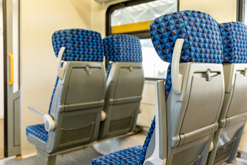 Back view. Interior of a modern train or bus with rows of blue seats, all unoccupied, and table....