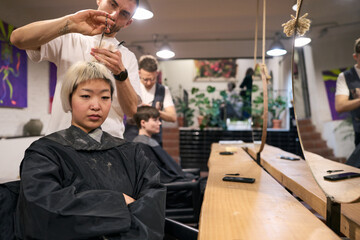 Hairdresser cutting hair of young female model in salon