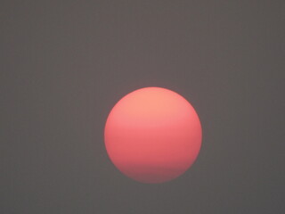 Red sun in the sky with white clouds on a gray background.