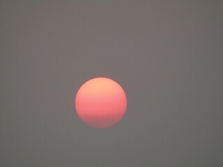 Red sun in the sky with white clouds on a gray background.