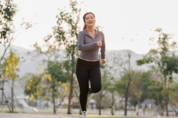 A young woman jogs purposefully in the city park, feeling joyful and energized, her mind uplifted by the refreshing atmosphere and soft sunlight.