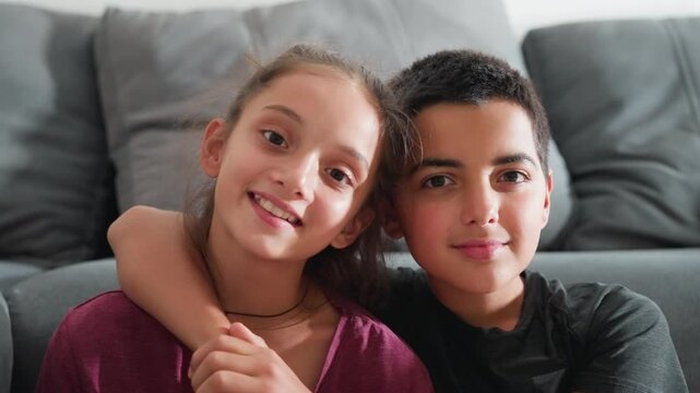 beautiful moment of siblings seated closely on couch smiling warmly with arms around each other showing strong bond and affection in cozy home setting with natural light