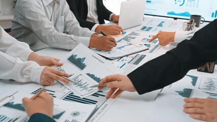 A diverse team engages in a collaborative business meeting, analyzing various graphs and charts to enhance strategic planning and financial performance in a modern office setting. SACTR