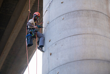 Rope access technician working on bridge concrete pillar using power drill