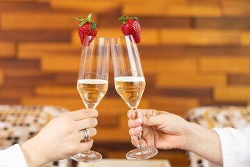 Two glasses of sparkling champagne with strawberries are raised, capturing a celebratory moment in a relaxing spa environment.
