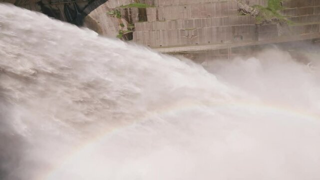 Floodgate opening of hydro dam unleashing powerful water stream and colorful rainbow, representing strength, water force, energy production.