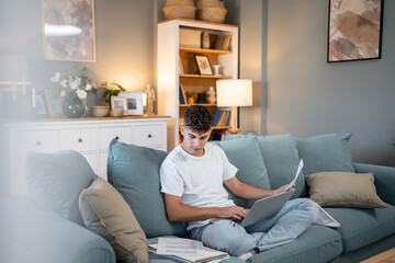 Obraz premium Focused student studying on sofa with laptop and documents at home