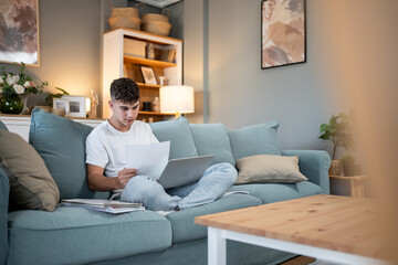 Obraz premium Focused student studying on sofa with laptop and documents
