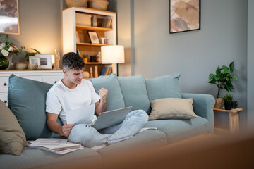 Obraz premium Young man celebrating success while working from home on laptop