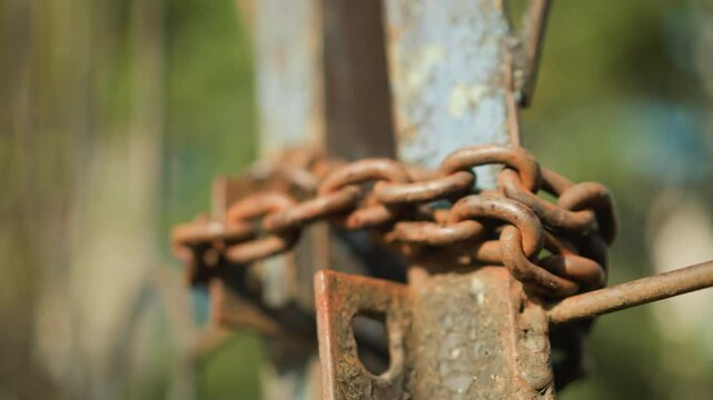Rusty chain used to lock gate with green blur background, capturing weathered metal links, sense of security in warm sunlight, focusing on heavily worn iron loops, patina texture, and aged surface
