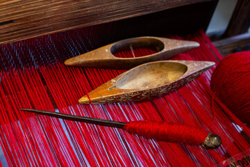 wooden weaving shuttles on an old hand loom. Close-up view of a traditional loom with red thread and wooden spoons