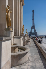 Paris, France - 03 31 2025: Trocadero Esplanade. Golden Statues of women at Palais de Chaillot and Eiffel Tower Montparnasse Tower behind.