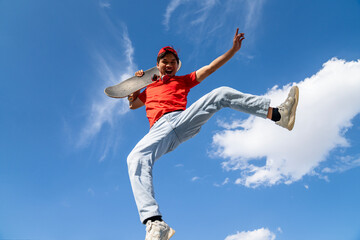 A man is jumping in the air with his arms outstretched. The sky is blue and there are clouds in the background. Scene is joyful and energetic
