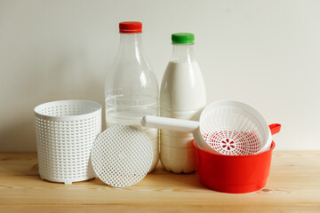Plastic equipment for making soft cheese and cottage cheese at home. A white uniform, a red ladle and two bottle of milk.