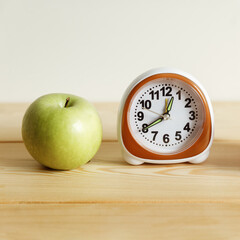 A green apple and a white small alarm clock on a light background.