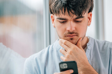 portrait of a young man or student with a mobile phone and a thoughtful expression of doubt or...