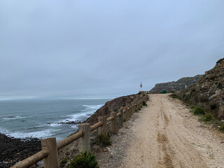 Coastal dirt path by the ocean with overcast sky, perfect for nature walks, summer exploration,...