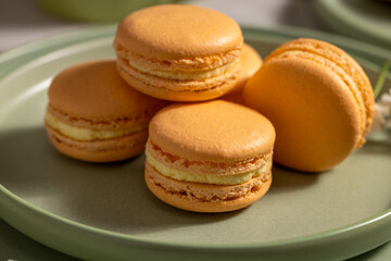 Delicious orange macarons resting on green plate
