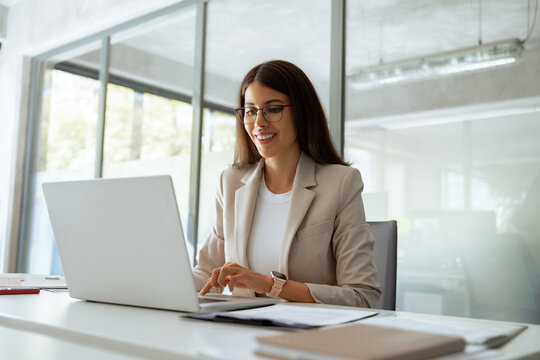 Smiling middle aged business woman using laptop at work in office. Professional female executive entrepreneur in suit working on computer pc at company workplace, doing financial analyze. Copy space