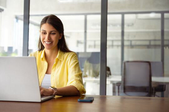 Smiling young indian business woman, it specialist using laptop at work in office. Female freelance entrepreneur working on online technological project on computer pc at company workplace. Copy space