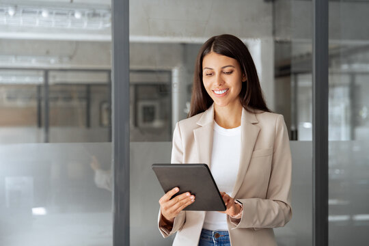Busy executive CEO businesswoman professional holding digital tablet pc device for work in modern office workplace. Successful smiling latin hispanic young woman using pad computer for business app