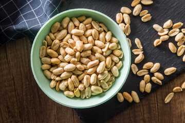 Roasted salted peanuts in bowl on wooden table. Top view.
