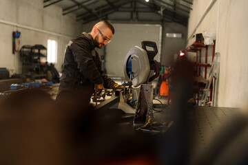 Professional metalworker wearing protective glasses and gloves operating a circular saw to cut a metal profile, demonstrating precision and skill in a workshop environment