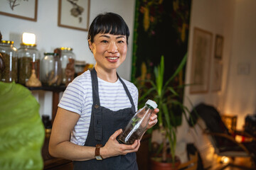 Portrait of japanese woman wear apron hold bottle in herbal workshop