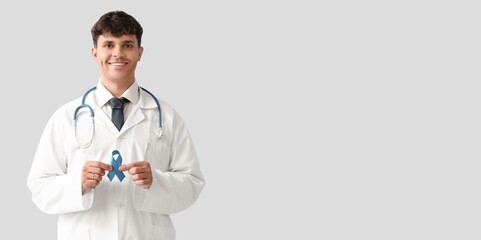 Male doctor with prostate cancer awareness ribbon on light background with space for text