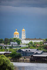 Fototapeta premium A picturesque town lush greenery, and golden-domed churches in the background. The dramatic sky adds contrast, creating a serene yet moody atmosphere.