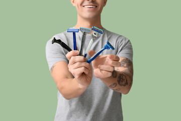 Handsome young man with razors after shaving on green background