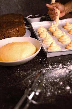 Pastry chef using a piping bag with freshly prepared cream to make desserts, alongside bread dough and a chocolate cake, a home-cooked artisanal cooking concept.
