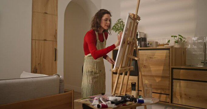 Brunette woman draws a picture on canvas using her fingers and paint at home