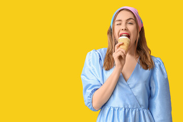 Young woman biting ice cream in waffle cup and winking on yellow background