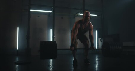 Man sweaty muscular athlete with beard and shaved head doing deadlift with big weights on dumbbells in gray gym