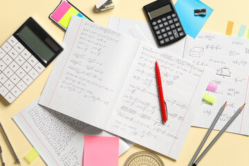 Copybooks with handwritten maths formulas and stationery on yellow background