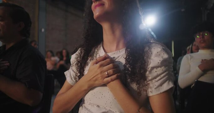 Woman with hands clasped in worship, head tilted back, deeply engaged in spiritual moment, illuminated cross in background, church setting, emotional expression
