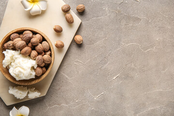 Bowl of shea butter with nuts and plumeria flowers on grey background