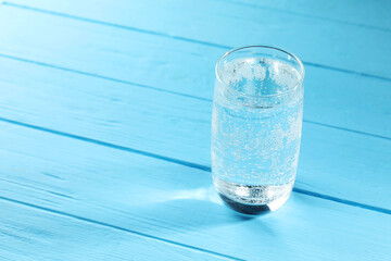 Refreshing soda water in glass on light blue wooden table, closeup. Space for text