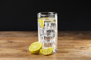 Fototapeta premium Refreshing soda water with ice cubes in glass and cut lemon on wooden table against black background