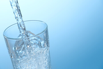 Pouring soda water into glass on light background, closeup. Space for text
