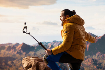 Influencer recording a video in the mountains sharing his outdoor journey with his audience. Male adult trekker always connected with a smartphone placed on a stabilizing tripod.