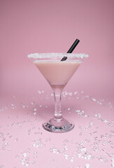 A pink drink in a martini glass with sugar around the rim, set against a light pink background. The soft, pastel tones of the drink and background.