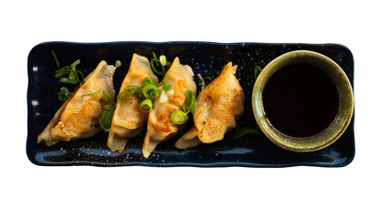 Image of Japanese tasty dumplings gyozas with bowl of soy sauce served on black plate. Isolated over white background
