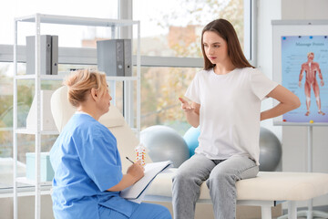 Fototapeta premium Young woman visiting mature female osteopath with clipboard in clinic
