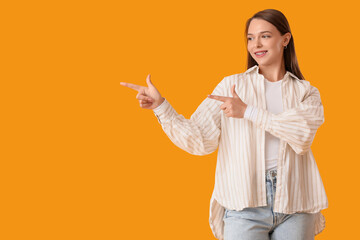 Beautiful happy young woman pointing at something on yellow background