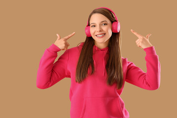 Beautiful young happy woman pointing at headphones on brown background
